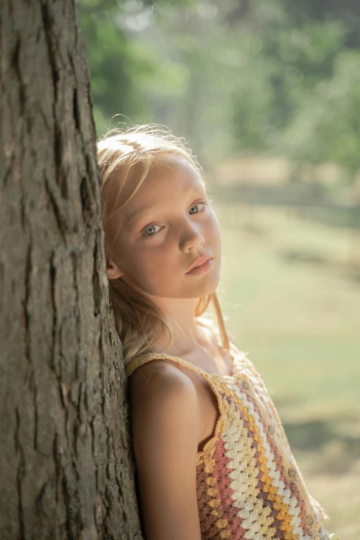 a young girl leaning against a tree trunk, inspired by Sophie Anderson, unsplash, portrait image, movie filmstill, pouty, kids