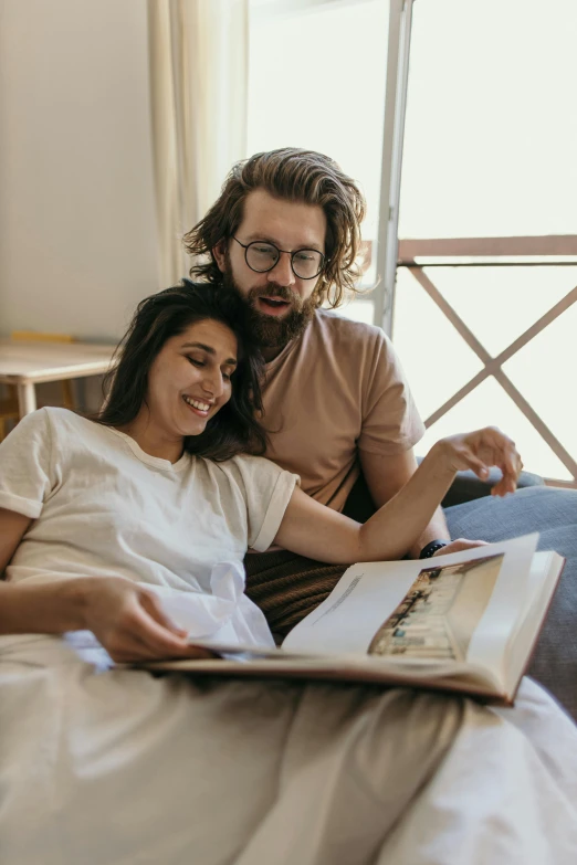 a man and woman sitting on a bed reading a book, a colorized photo, pexels contest winner, hipster dad, australian, maternity feeling, gif