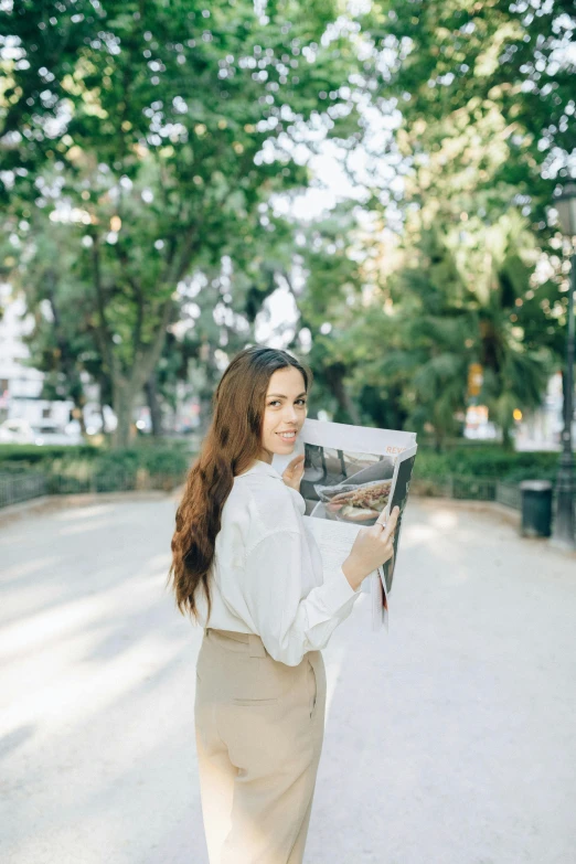 a woman walking down a street holding a newspaper, pexels contest winner, realism, wearing a white blouse, at a park, maxim shirkov, with long hair