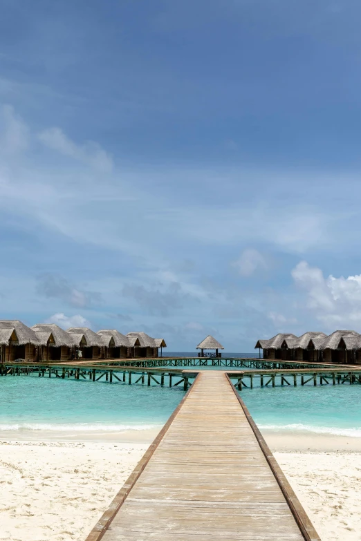 a wooden walkway leading to a beach with thatched huts, hurufiyya, infinity concentric pool, slide show, square