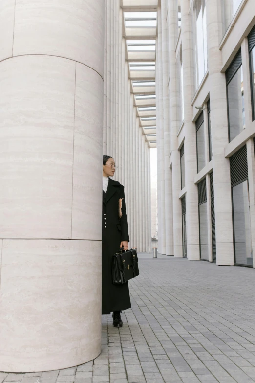 a man standing in front of a tall building, an album cover, inspired by Wang E, pexels contest winner, baroque, woman in black business suit, wearing a long coat, pillars of marble, berlin fashion