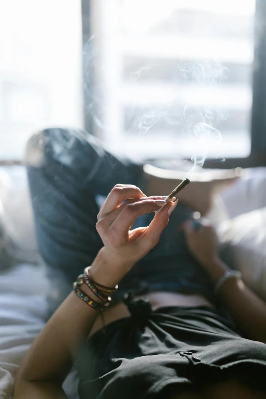 a woman laying on a bed smoking a cigarette, trending on pexels, smoking a bowl of hash together, phone in hand, sage smoke, low fi