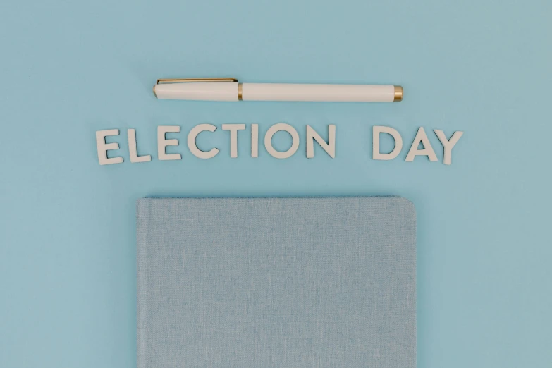 a book sitting on top of a table next to a pen, by Ellen Gallagher, verdadism, election poster, white and pale blue toned, day time, celebration