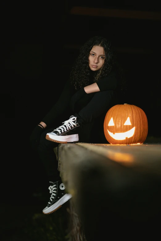 a woman sitting on a ledge next to a pumpkin, a portrait, pexels, antipodeans, standing with a black background, sneaker photo, with haunted eyes and curly hair, teenager