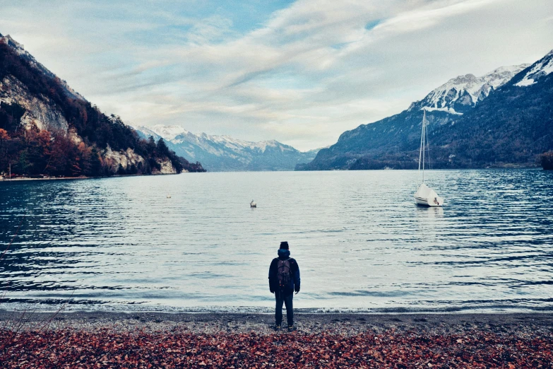 a person standing on a beach next to a body of water, inspired by Thomas Struth, pexels contest winner, visual art, lakeside mountains, switzerland, videogame still, a very sad man