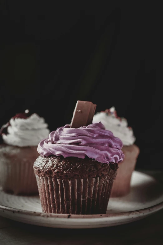 three cupcakes with purple frosting on a plate, a colorized photo, pexels, chocolate. rugged, ((purple)), dark and white, on