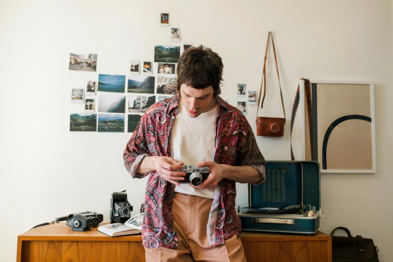 a man standing in front of a dresser holding a camera, a picture, by Terese Nielsen, pexels contest winner, joe keery, patterned clothing, artist wearing overalls, tourist photo