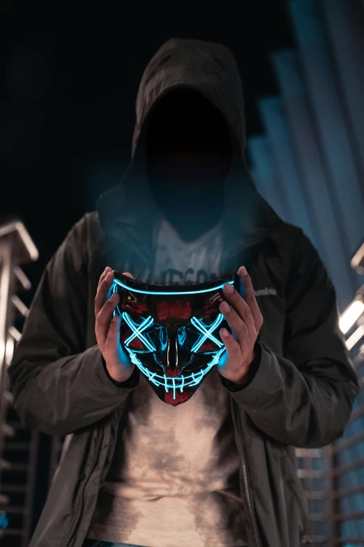 a man in a hoodie holding a glowing mask, an album cover, trending on pexels, leds visor helmet, modded, avatar image, glowing wires