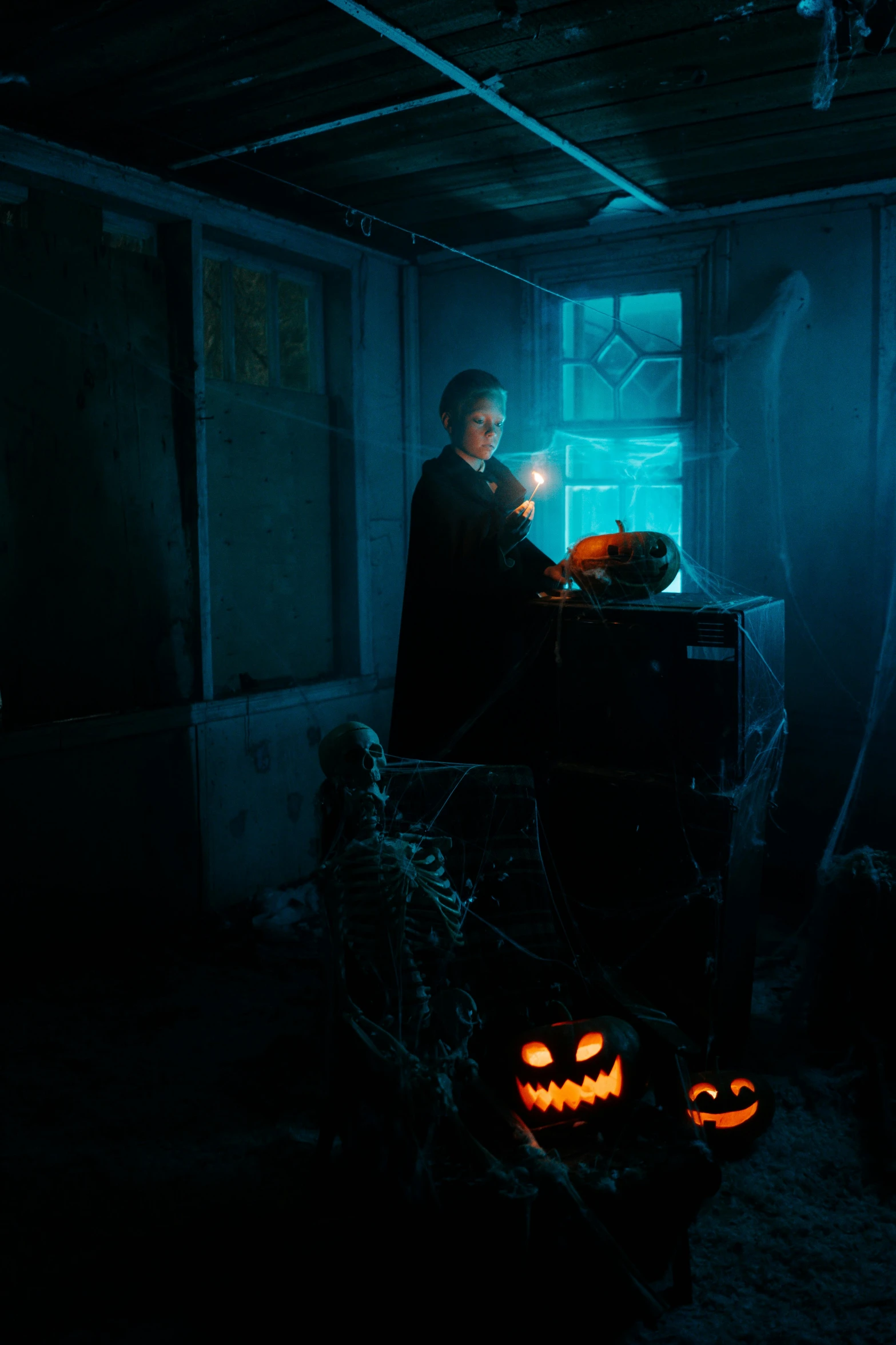 a man sitting at a table in a dark room, pexels, vanitas, holding a jack - o - lantern, wizard holding a cage, dark teal lighting, animatronic