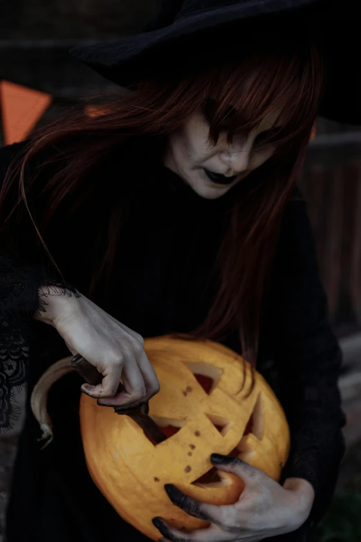a woman in a witch costume holding a pumpkin, inspired by Nicola Samori, pexels contest winner, gothic art, carving, low quality photo, profile image, readhead