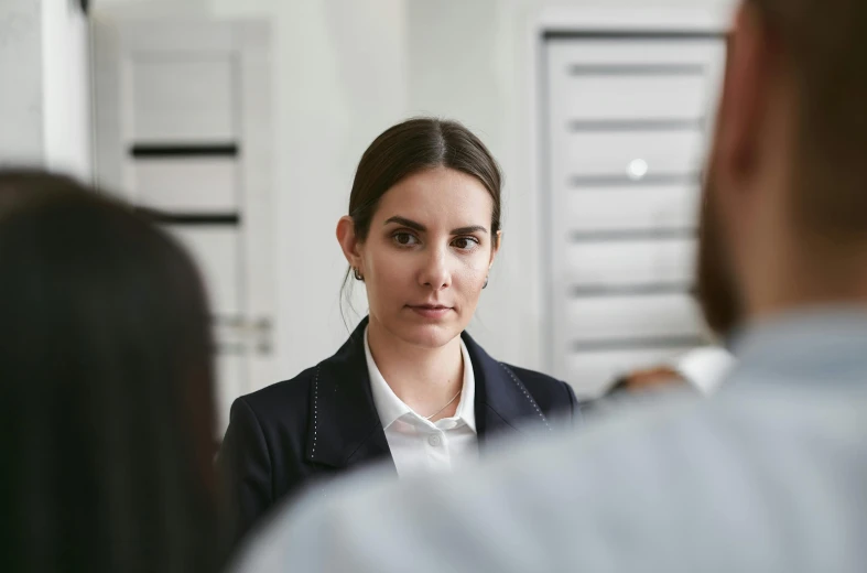 a woman standing in front of a man in a suit, complaints, woman holding another woman, headshot, female in office dress