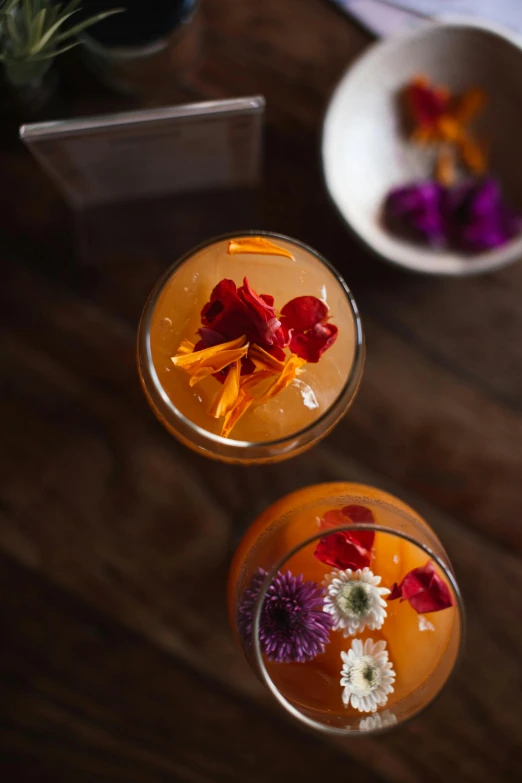 a couple of glasses sitting on top of a wooden table, edible flowers, speakeasy, mango, f / 2 0