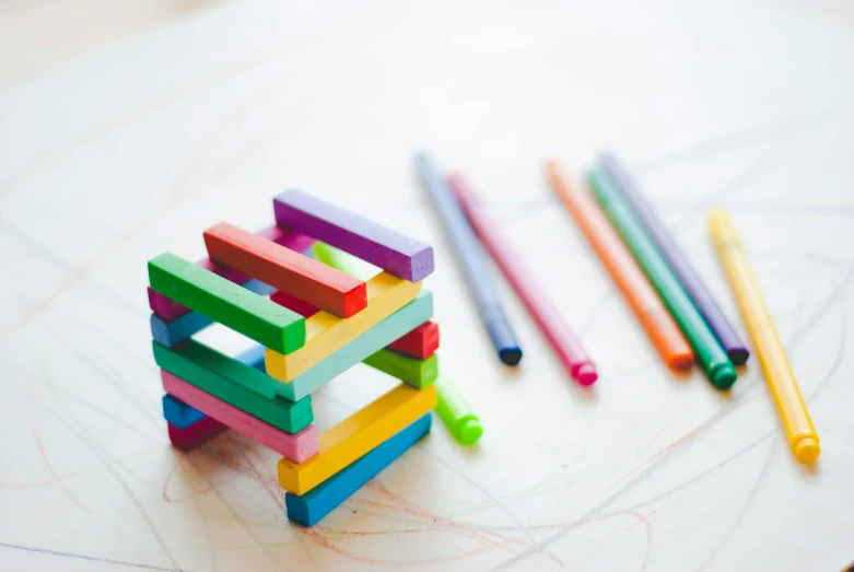 a stack of colored pencils sitting on top of a table, a child's drawing, inspired by Joel Shapiro, pexels contest winner, square shapes, jenga tower, wooden art toys