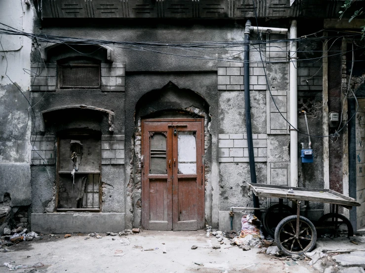 an old building with a cart in front of it, by Abdullah Gërguri, pexels contest winner, doors to various living quarters, after a riot, grey, with an intricate