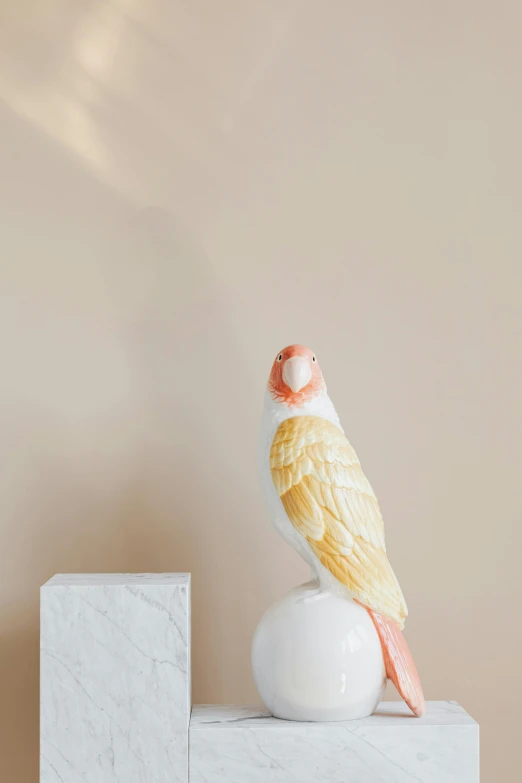 a yellow bird sitting on top of a white ball, a marble sculpture, by Lucette Barker, trending on pexels, light red and orange mood, ethereal macaw, detailed product image, white porcelain skin