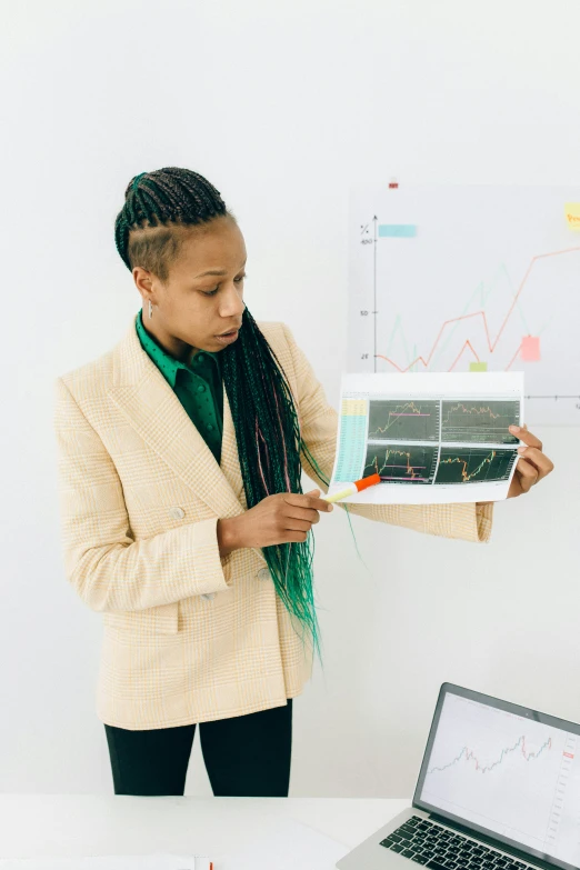 a woman holding a piece of paper in front of a laptop, analytical art, wearing green suit, graphs, teaching, realistic »