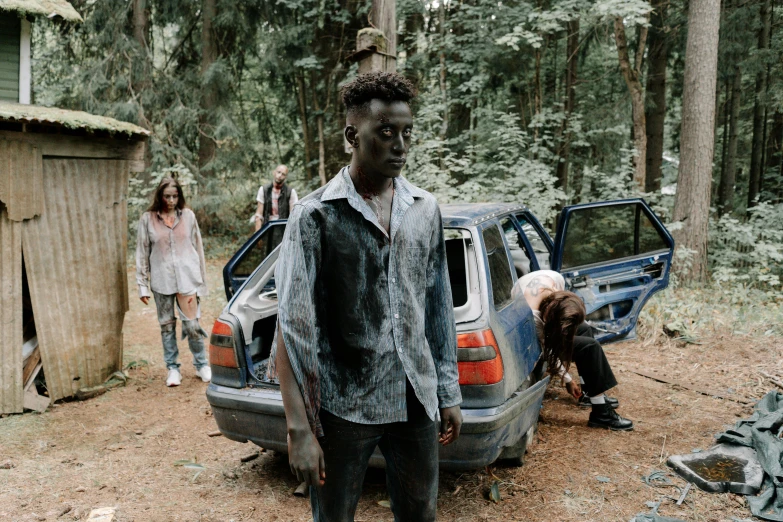 a man standing next to a car in a forest, an album cover, pexels contest winner, auto-destructive art, zombie ghouls, black teenage boy, a group of people, [ theatrical ]