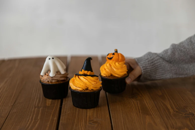 a group of cupcakes sitting on top of a wooden table, by Emma Andijewska, pexels, trick or treat, back of hand on the table, high resolution product photo, small in size