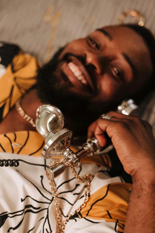 a man laying on a couch talking on a cell phone, an album cover, inspired by Ras Akyem, trending on pexels, happening, holding a scepter, smiling seductively, gold shirt, bearded