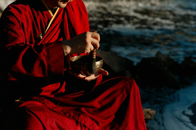 a man in a red robe sitting on a rock, pexels contest winner, mortar and pestle, holding a golden bell, avatar image, wearing dark silk robe