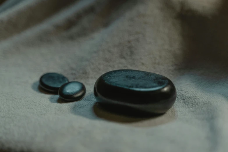 a couple of rocks sitting on top of a bed, unsplash, made of smooth black goo, buttons, black cloth, close-up photograph