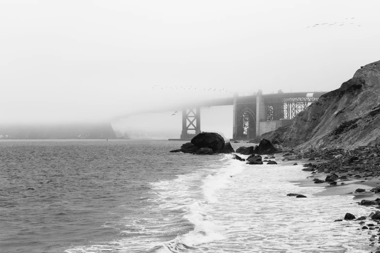 a black and white photo of the golden gate bridge, by Dave Melvin, pexels, sand mists, shoreline, 2 5 6 x 2 5 6 pixels, bridge over the water