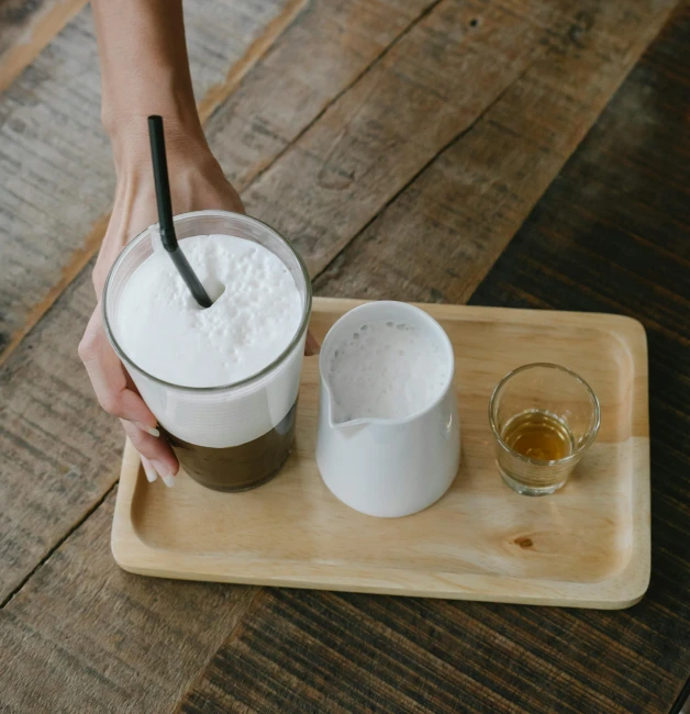 a person holding a spoon over a bowl of food, iced latte, on a wooden tray, white foam, multiple stories