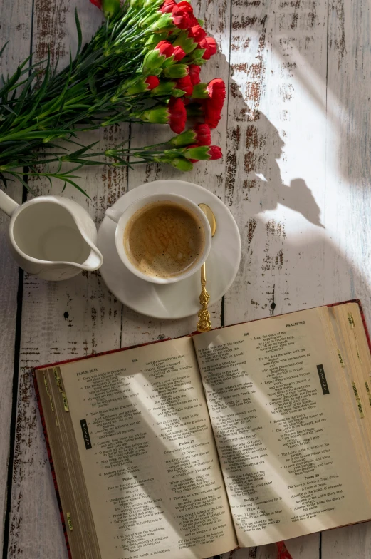 an open book sitting on top of a table next to a cup of coffee, religious, flowers around, breakfast, sunlit