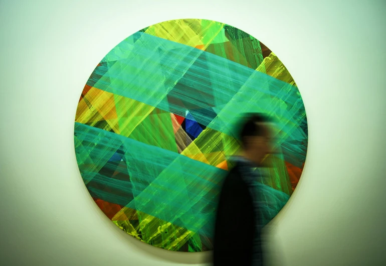 a person standing in front of a painting, by Damien Hirst, flickr, abstract art, circular, blue and green colours, walking to the right, peter saville