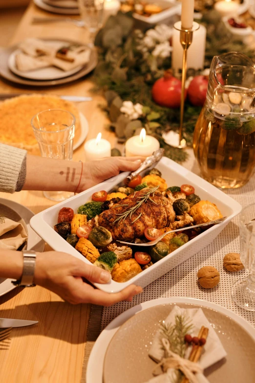 a close up of a person holding a tray of food, vegetables on table and candle, profile image, christmas night, square