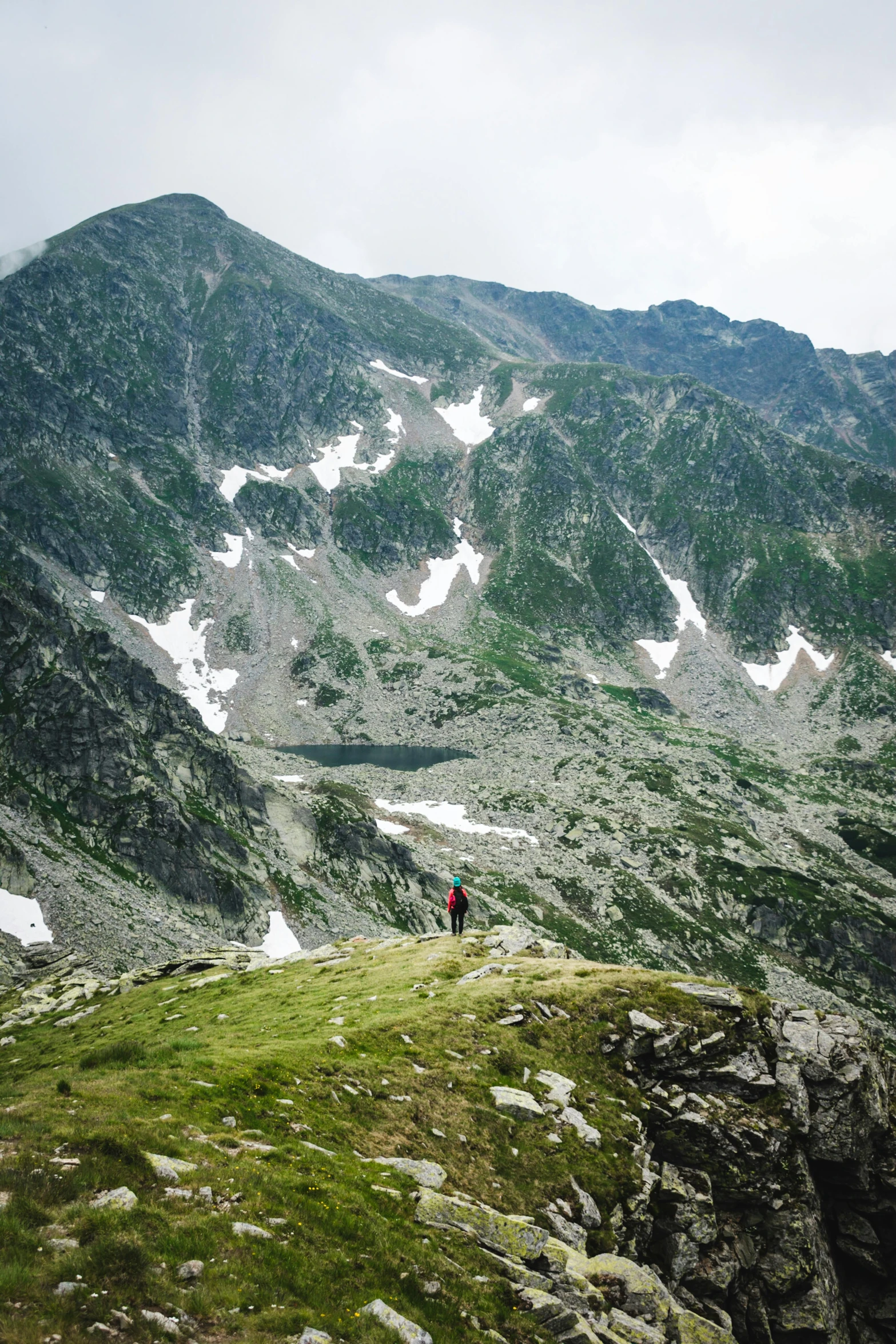 a man standing on top of a lush green hillside, by Emma Andijewska, snowy craggy sharp mountains, poland, multiple stories, hiking in rocky mountain