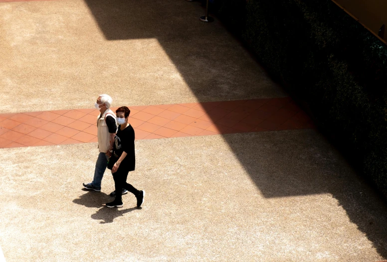 a couple of people walking down a sidewalk, by Bernie D’Andrea, pexels contest winner, conceptual art, black and terracotta, at college, partially masked, sunlit