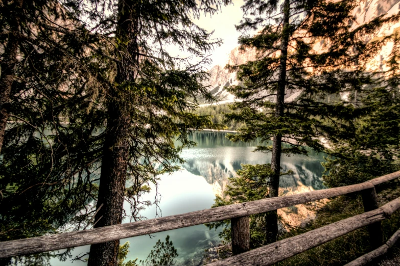 a wooden fence next to a body of water, by Sebastian Spreng, pexels contest winner, romanticism, spruce trees, banff national park, italy, post-processed