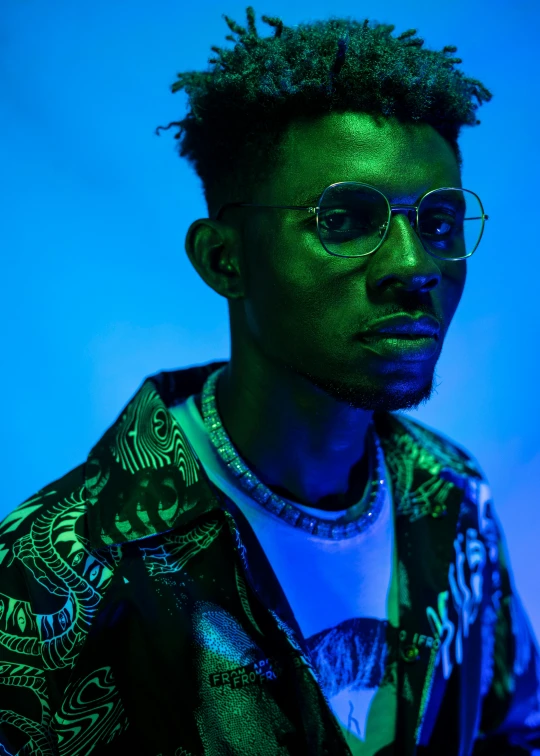 a man with glasses standing in front of a blue background, inspired by Philipp Veit, trending on pexels, afrofuturism, shot at night with studio lights, 2 1 savage, blue and green light, promotional image