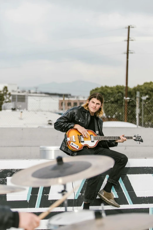 a man sitting on a bench playing a guitar, standing on a rooftop, hollywood promotional image, zac retz, beatle