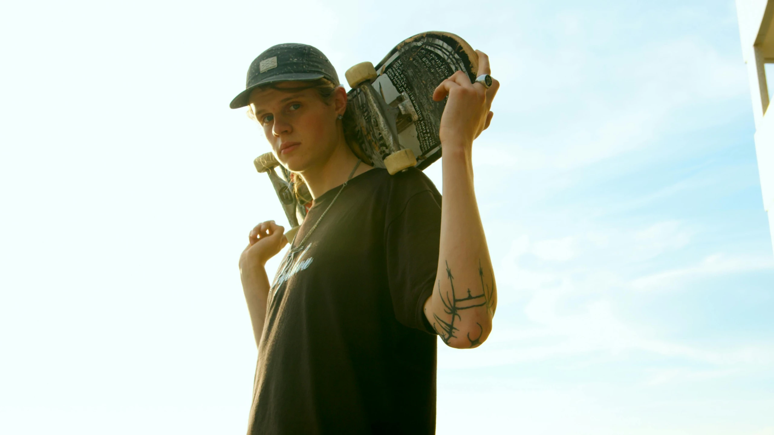 a man holding a skateboard over his shoulder, a picture, by Winona Nelson, eleven/millie bobbie brown, hand holding cap brim, press shot, summer evening