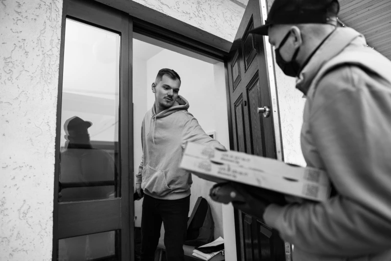 a man that is standing in front of a door, sharing a pizza, white man with black fabric mask, delivering parsel box, grayscale photography