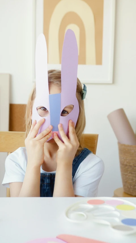 a little girl sitting at a table with a paper bunny mask on her face, pexels contest winner, visual art, 15081959 21121991 01012000 4k, purple, at home, made of paper