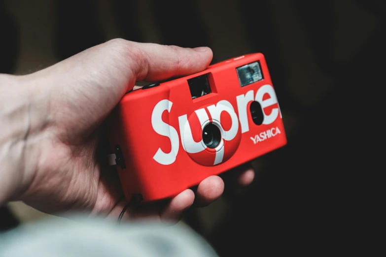 a person holding a red camera in their hand, inspired by Elsa Bleda, unsplash, supreme, toy photo, disposable camera, sup