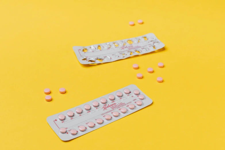 a couple of pills sitting on top of a yellow table, by Ellen Gallagher, trending on pexels, antipodeans, minimal pink palette, pair of keycards on table, contracept, ( ultra realistic