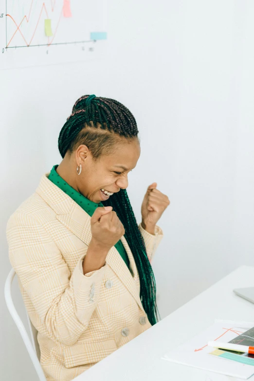 a woman sitting at a table in front of a laptop computer, pexels contest winner, standing triumphant and proud, cornrows, wearing green jacket, celebrate goal