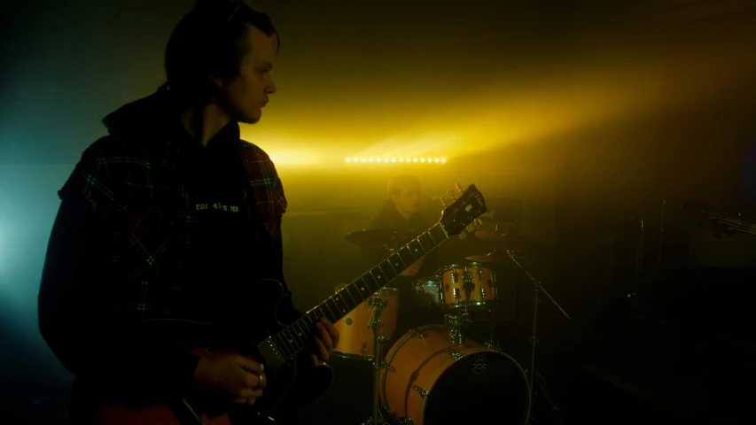 a man playing a guitar in a dark room, yellow lighting from right, band promo, hazy, movie still 8 k