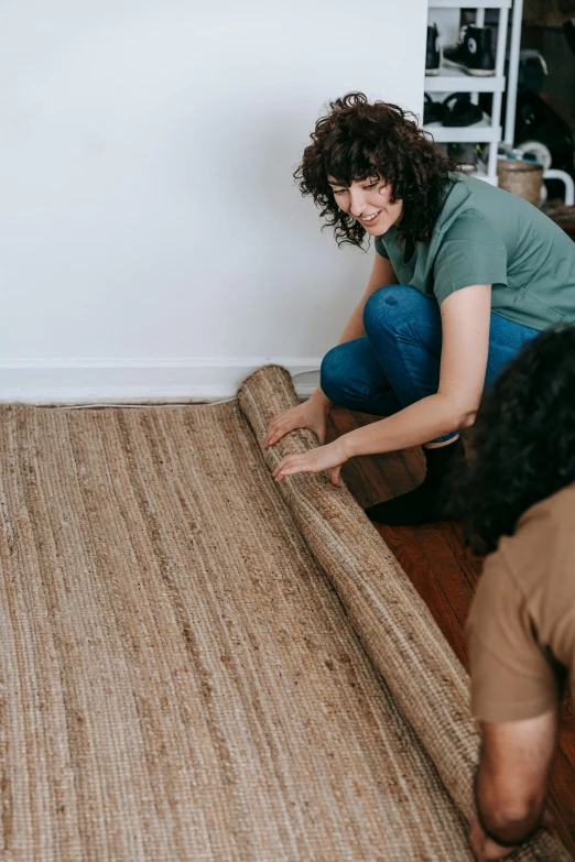 a woman laying a rug on top of a hard wood floor, by Carey Morris, trending on pexels, arts and crafts movement, medium shot of two characters, inspect in inventory image, natural materials, hemp