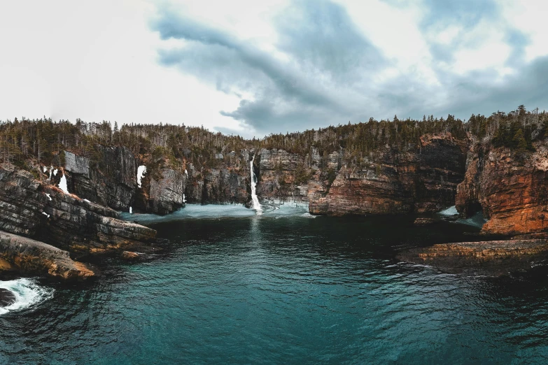 a body of water surrounded by rocks and trees, by Jesper Knudsen, pexels contest winner, hurufiyya, huge chasm, panoramic, thumbnail, high cliff