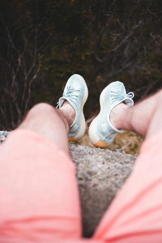 a person sitting on a rock with their feet up, short light grey whiskers, sneaker, wearing shorts, bumpy skin