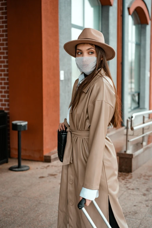 a woman wearing a face mask and holding a suitcase, by Julia Pishtar, trending on pexels, renaissance, light brown trenchcoat, beige fedora, wearing a full leather outfit, surgical mask covering mouth