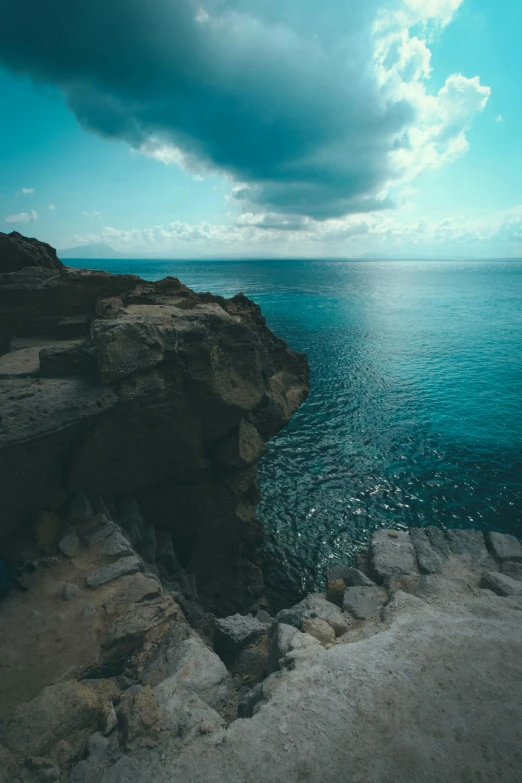 a large body of water next to a cliff, pexels contest winner, dramatic clouds cyan atmosphere, cyprus, dramatic”