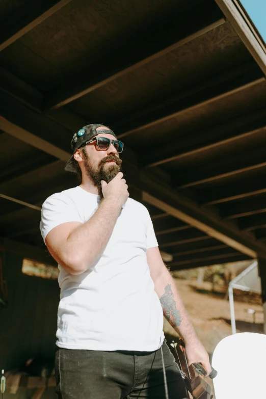 a man talking on a cell phone while holding a skateboard, unsplash, long goatee beard, in a cabin, shades, man in white t - shirt