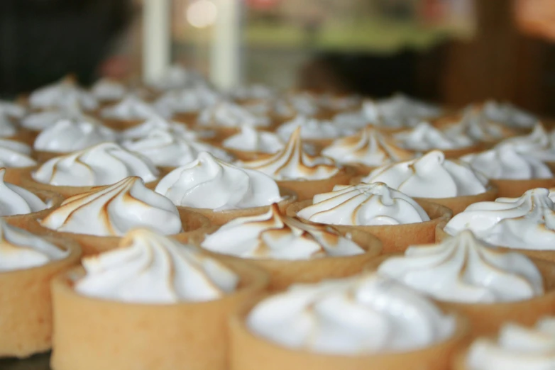 a table topped with lots of cupcakes covered in white frosting, by Lee Loughridge, trending on unsplash, pie eyes, in a row, caramel, mid closeup