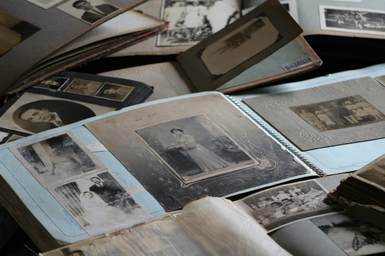 a pile of old photos sitting on top of a table, a black and white photo, by Jessie Algie, unsplash, process art, victorian photo, character sheets on table, blue archive, detailed photo of an album cover